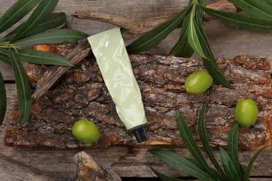 Photo of Tube of cream, olives and leaves on wooden table, flat lay