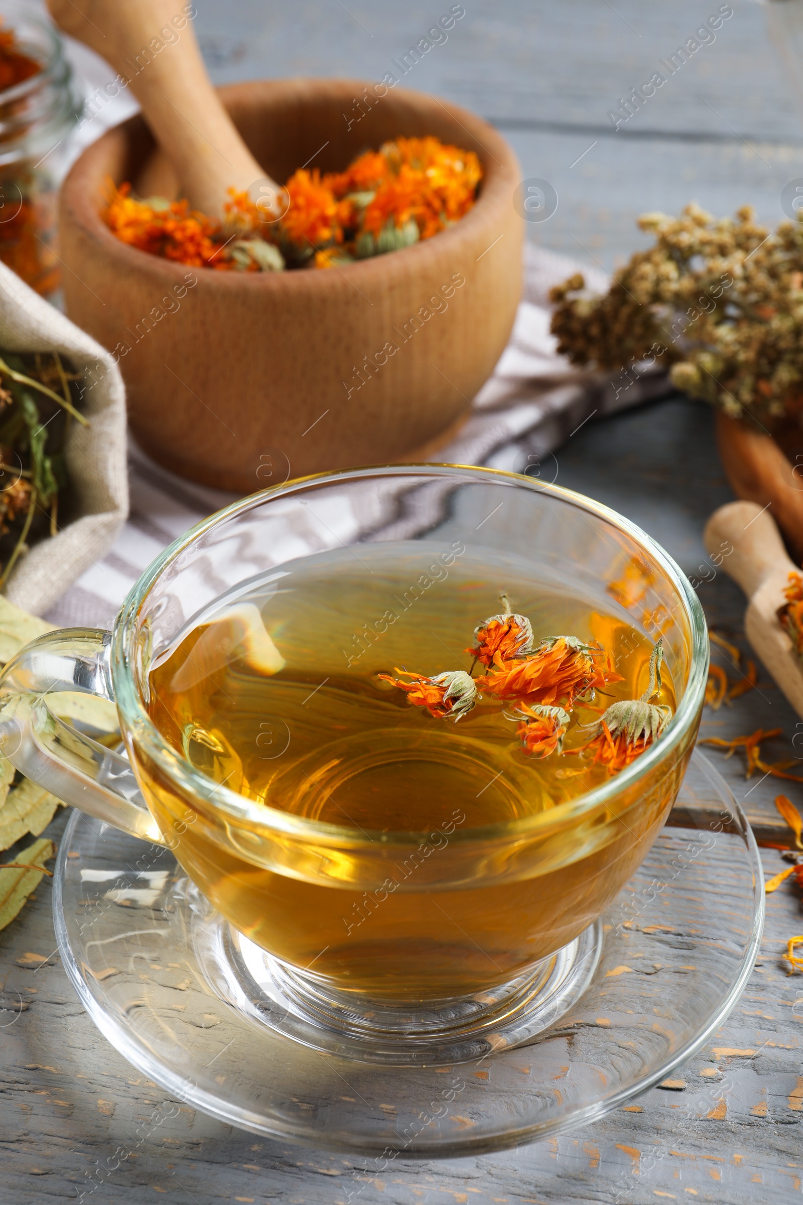 Photo of Freshly brewed tea and dried herbs on grey wooden table