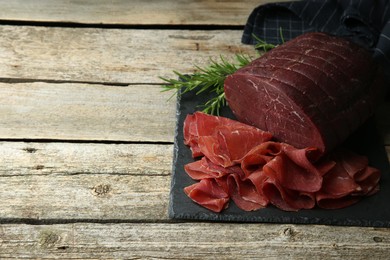 Photo of Tasty bresaola and rosemary on wooden table. Space for text