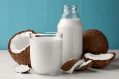 Photo of Glass and bottle of delicious vegan milk with coconuts on white marble table