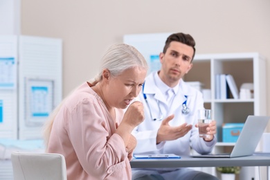 Photo of Coughing mature woman visiting doctor at clinic