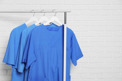 Photo of Medical uniforms hanging on rack near white brick wall. Space for text