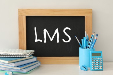 Learning management system. Small chalkboard with abbreviation LMS on light table with stationery