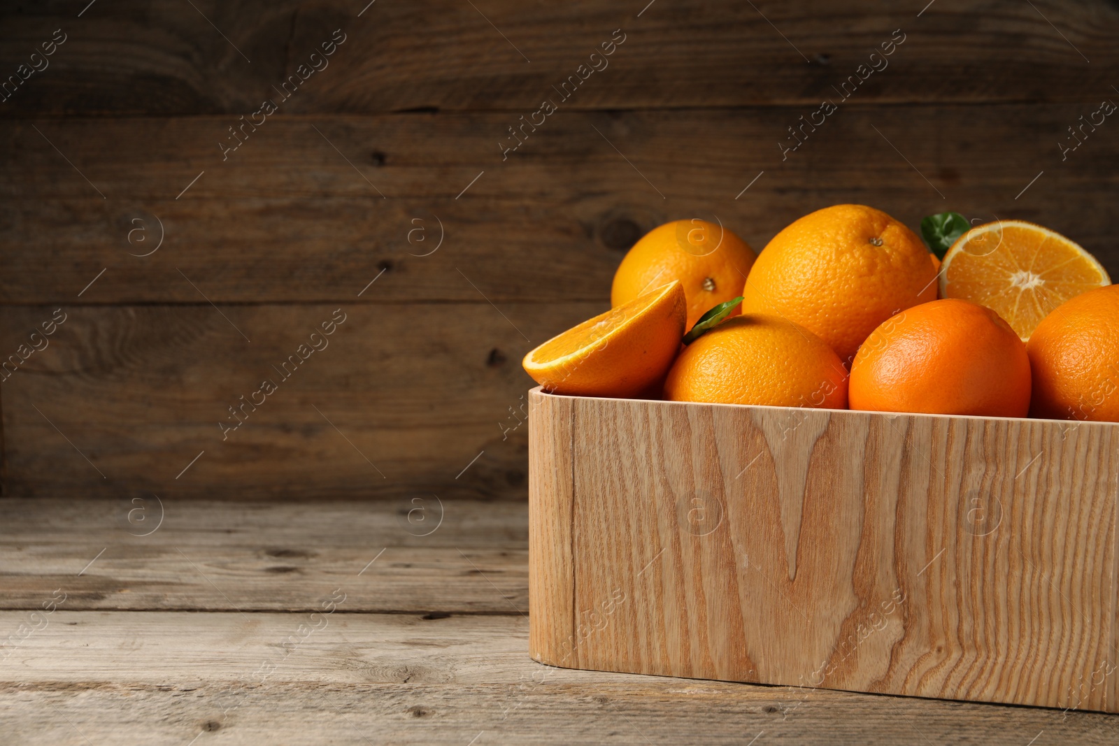 Photo of Many whole and cut ripe oranges on wooden table, space for text