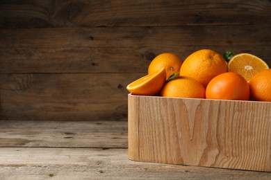 Photo of Many whole and cut ripe oranges on wooden table, space for text