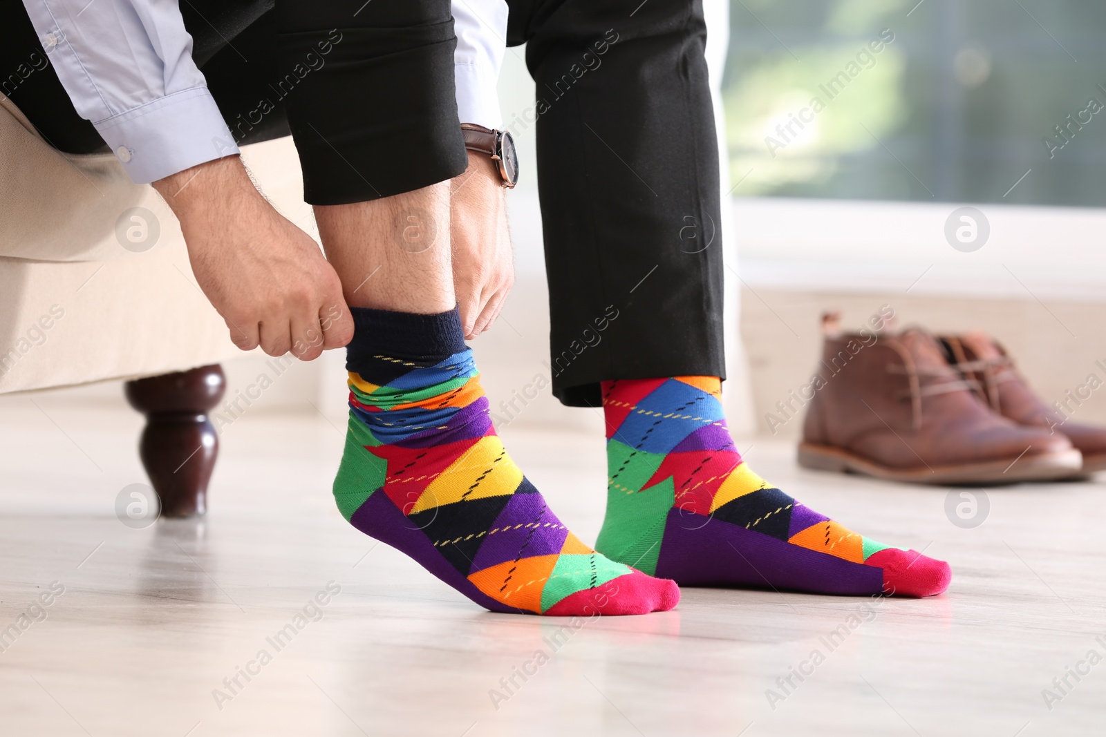 Photo of Man putting on stylish socks indoors, closeup