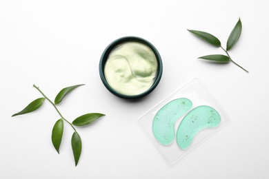 Photo of Different under eye patches and green twigs on white background, flat lay. Cosmetic product