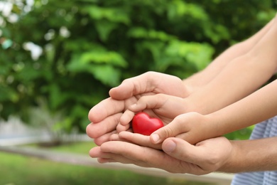 Photo of Family holding small red heart in hands together outdoors, closeup
