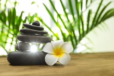 Photo of Table with stack of stones, flower and blurred green leaves on background, space for text. Zen concept