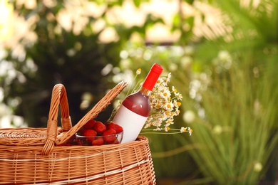 Picnic basket with wine, strawberries and flowers on blurred background, space for text