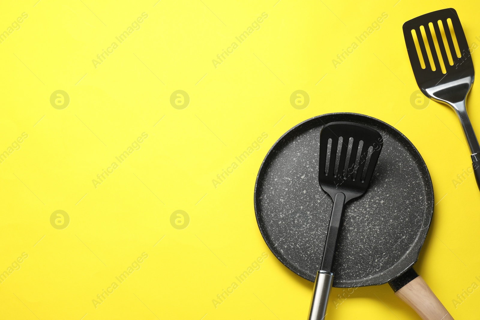 Photo of Spatulas and frying pan on yellow background, flat lay. Space for text