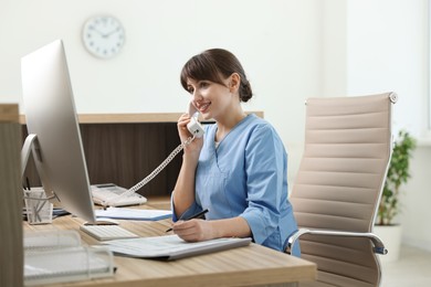 Photo of Smiling medical assistant talking by phone in office