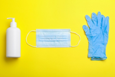 Medical gloves, mask and hand sanitizer on yellow background, flat lay