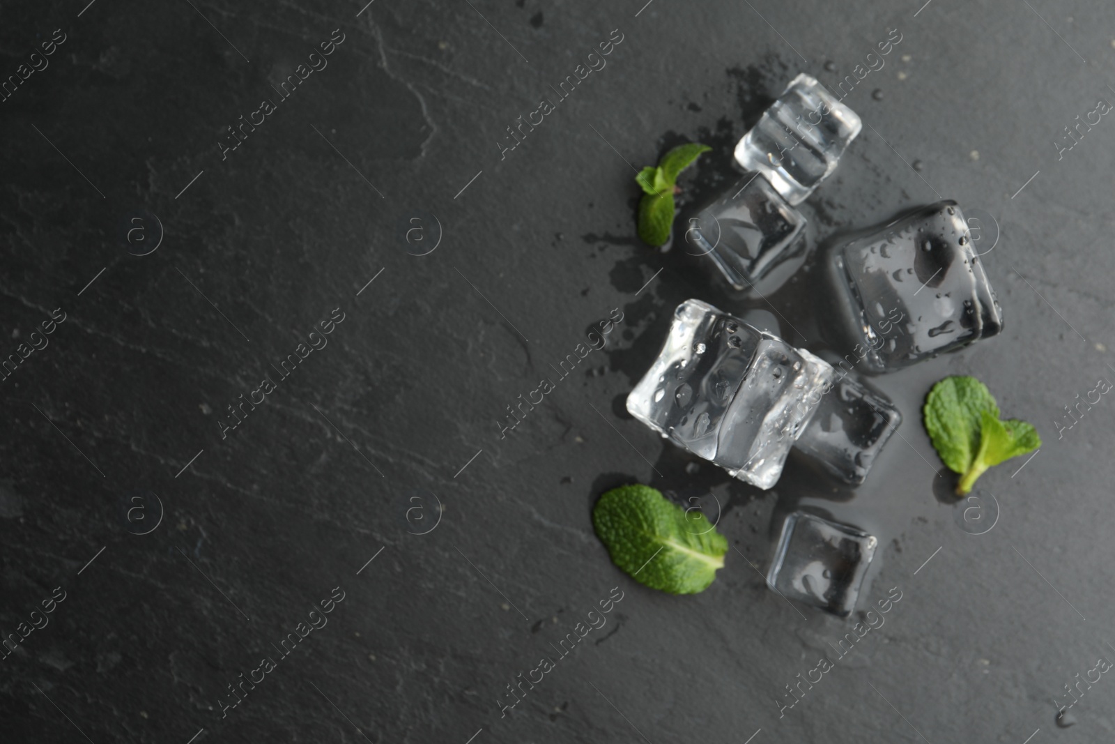 Photo of Crystal clear ice cubes with water drops and mint on black table, flat lay. Space for text