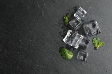 Photo of Crystal clear ice cubes with water drops and mint on black table, flat lay. Space for text