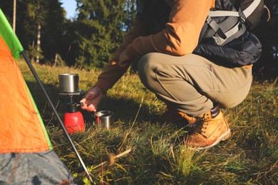 Photo of Man making hot drink with portable gas burner near camping tent, closeup