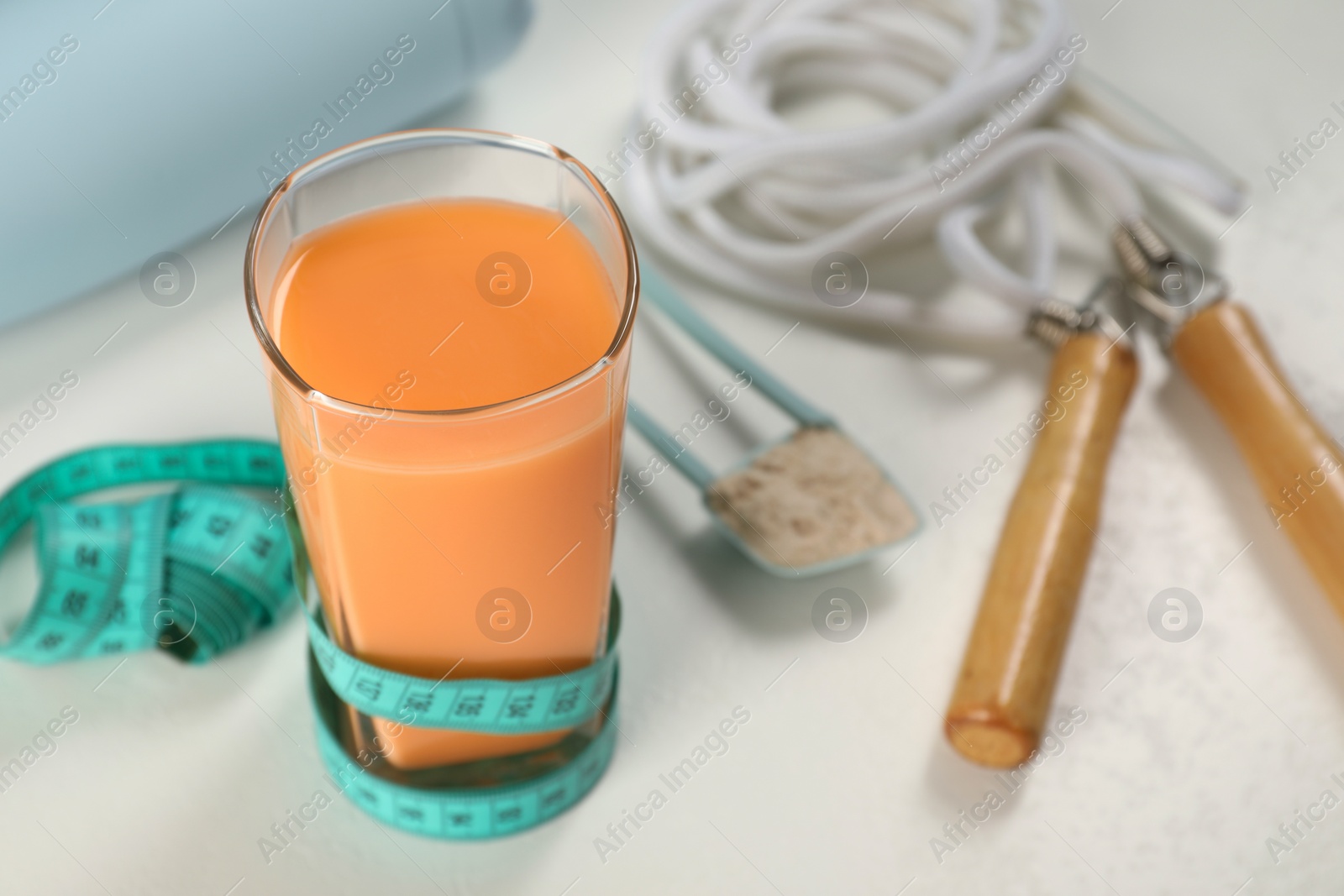 Photo of Tasty shake, measuring tape skipping rope and powder on light table, closeup. Weight loss