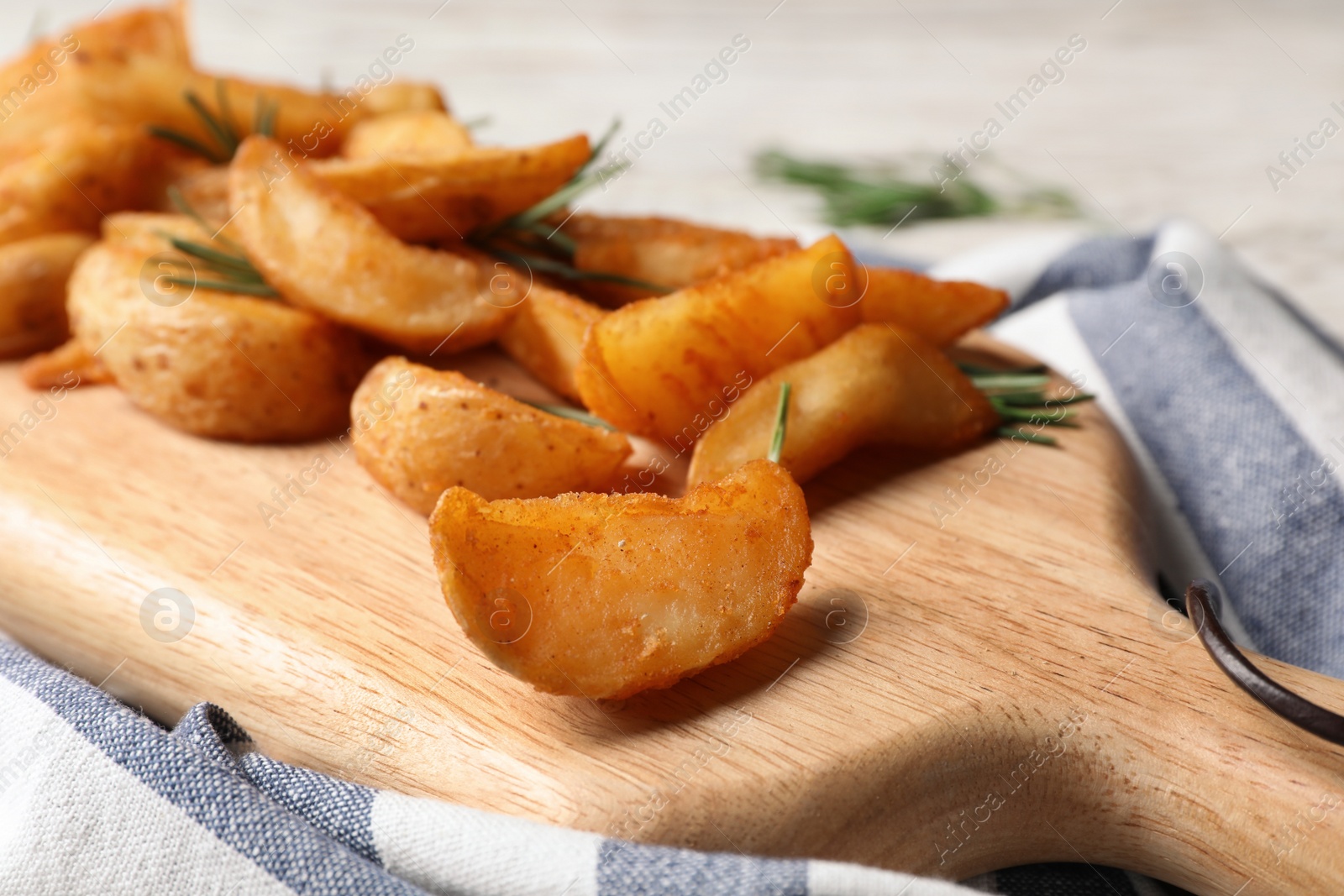 Photo of Wooden board with baked potatoes and rosemary on table, closeup