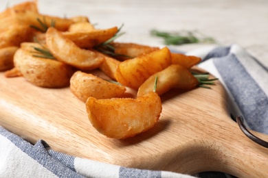 Photo of Wooden board with baked potatoes and rosemary on table, closeup