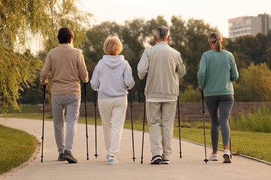 Photo of Group of senior people performing Nordic walking outdoors, back view