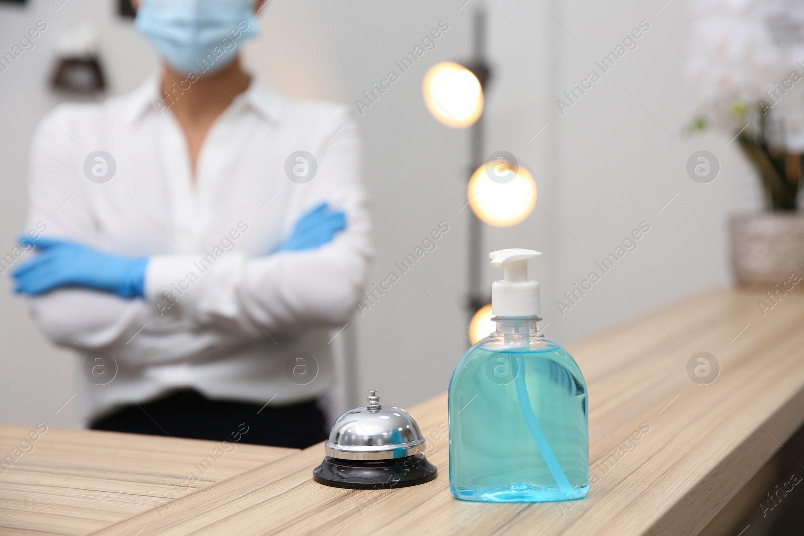 Photo of Receptionist at countertop in hotel, focus on dispenser bottle with antiseptic gel and service bell