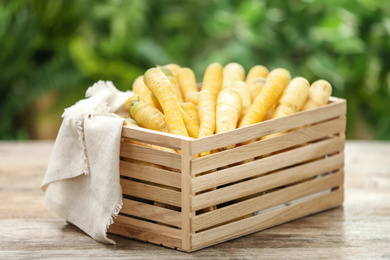 Photo of Raw white and yellow carrots in crate on wooden table against blurred background