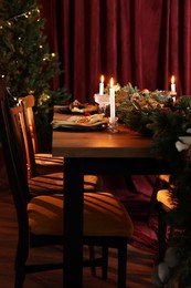 Dining table with burning candles and Christmas decor in stylish room. Interior design