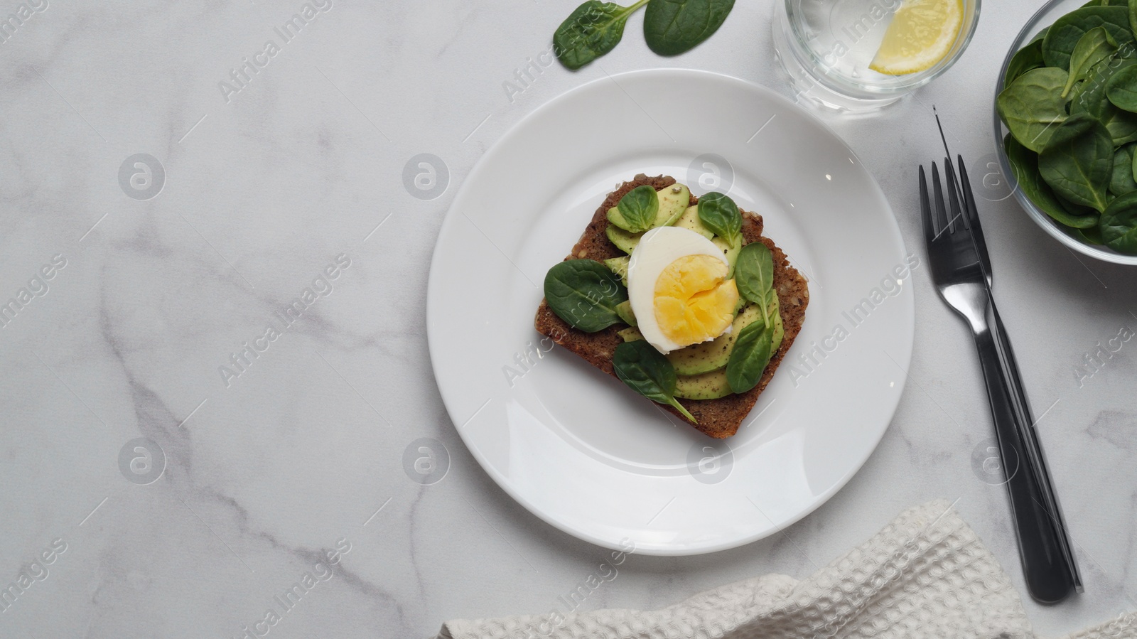 Photo of Tasty sandwich with boiled egg, avocado and spinach served on white marble table, flat lay. Space for text