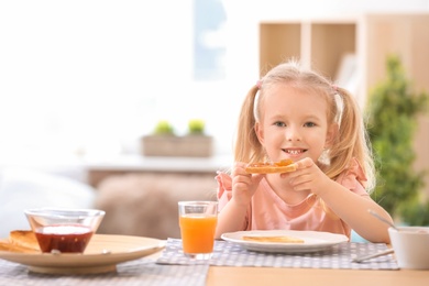 Photo of Cute little girl eating tasty toasted bread with jam at table