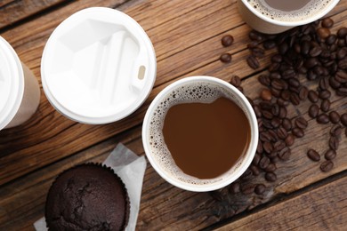 Coffee to go. Paper cups with tasty drink, muffin and beans on wooden table, flat lay