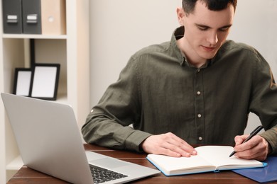 Photo of Man taking notes at wooden table in office