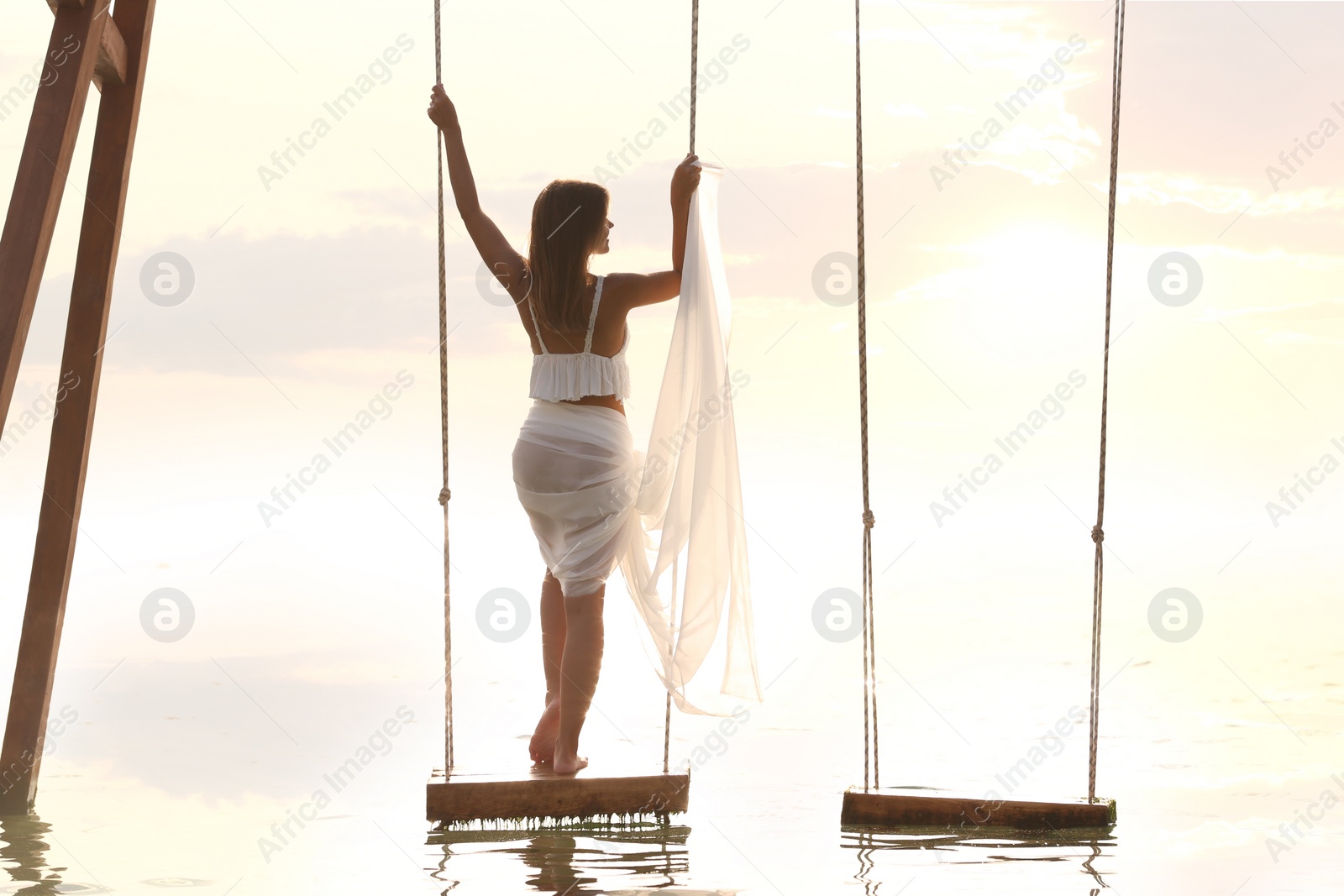 Photo of Young woman enjoying sunrise on swing over water