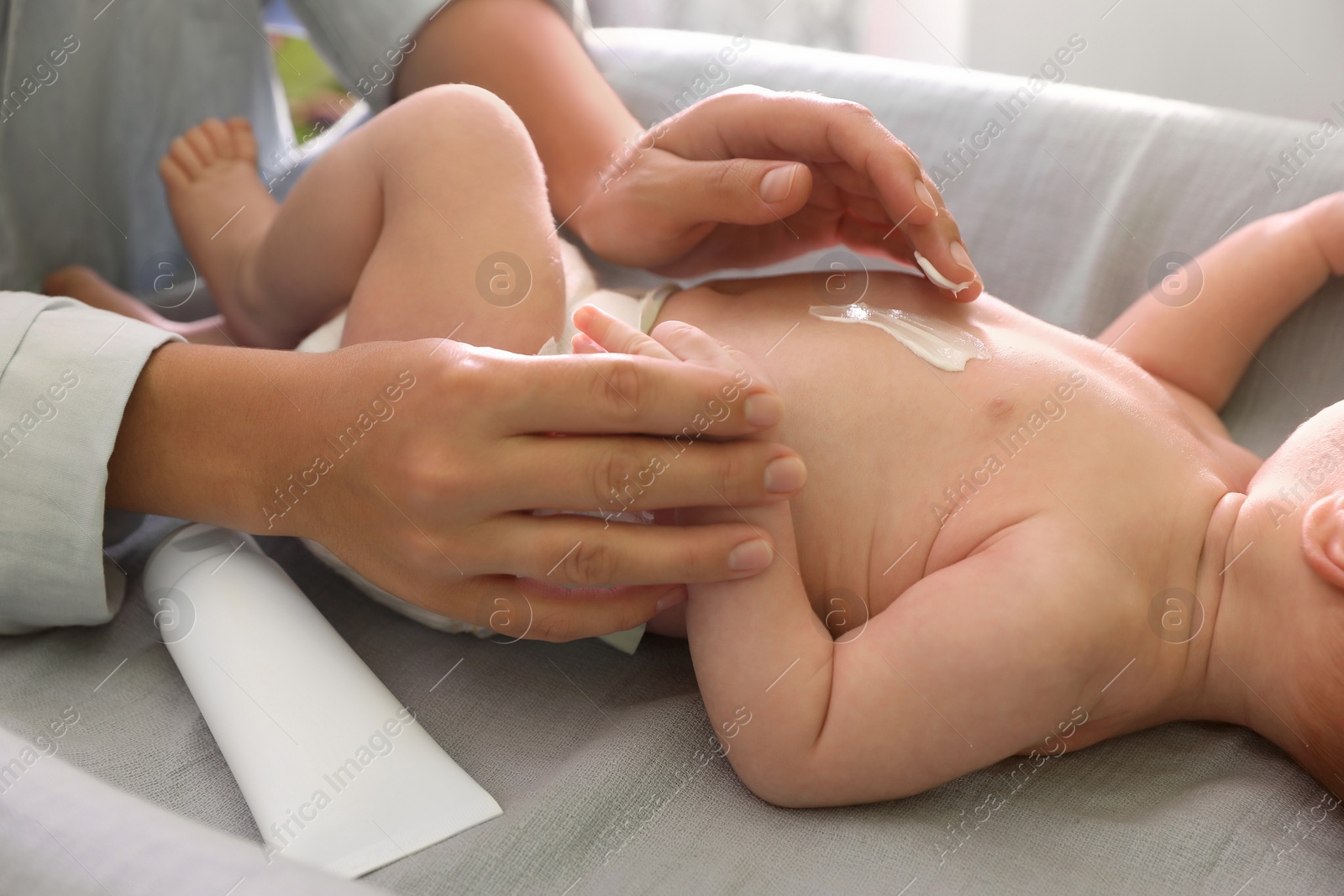 Photo of Mother applying moisturizing cream onto baby`s skin on changing table indoors, closeup