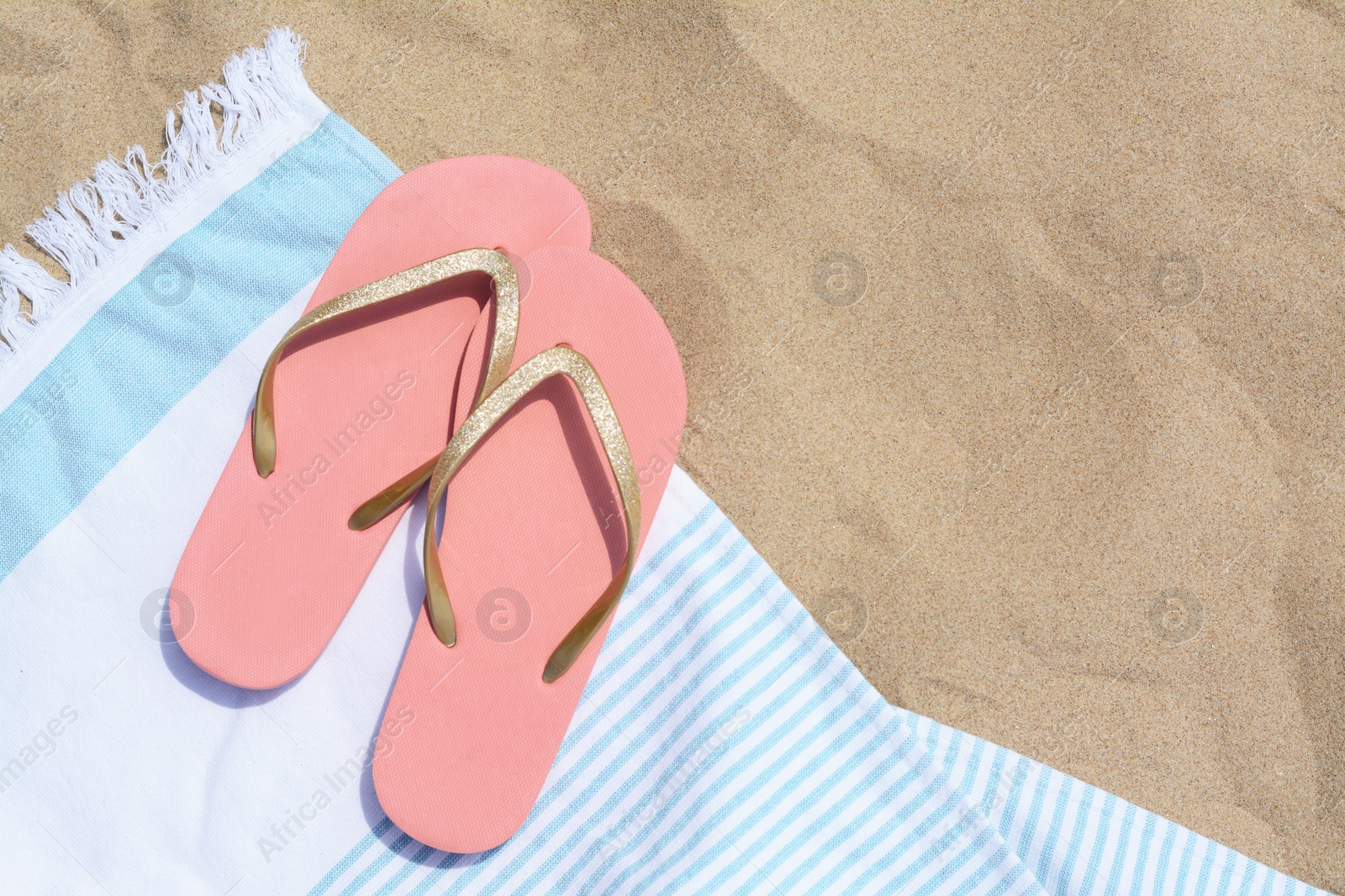 Photo of White and light blue striped towel with flip flops on sandy beach, flat lay. Space for text