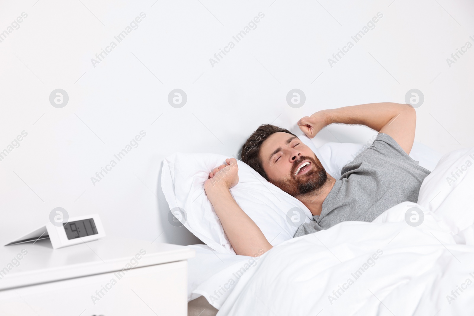 Photo of Happy man stretching on comfortable pillow in bed at home