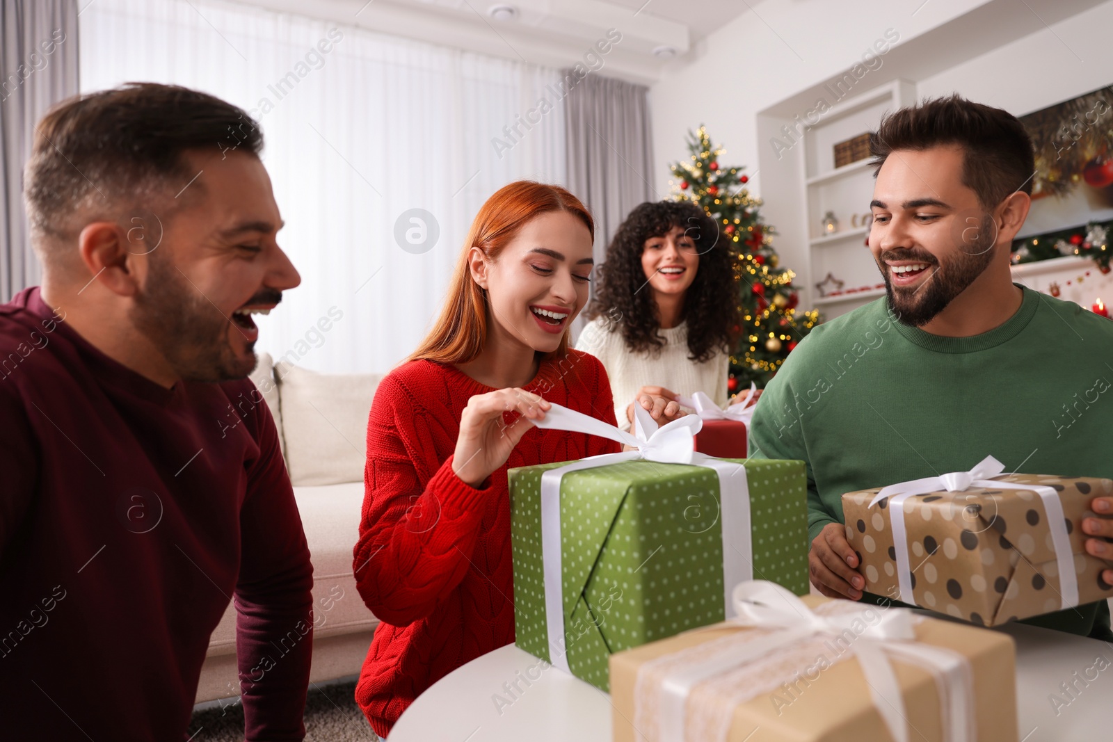 Photo of Christmas celebration in circle of friends. Happy woman opening gift at home