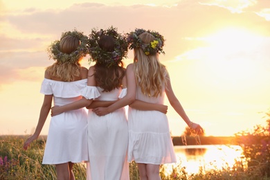 Photo of Young women wearing wreaths made of flowers outdoors at sunset, back view