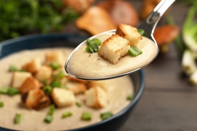 Photo of Spoon with fresh homemade mushroom soup over bowl, closeup