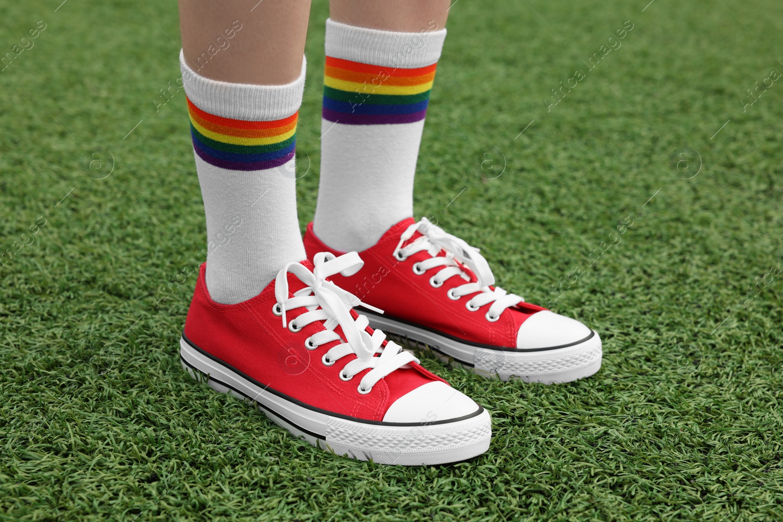 Photo of Woman wearing red classic old school sneakers on green grass outdoors, closeup