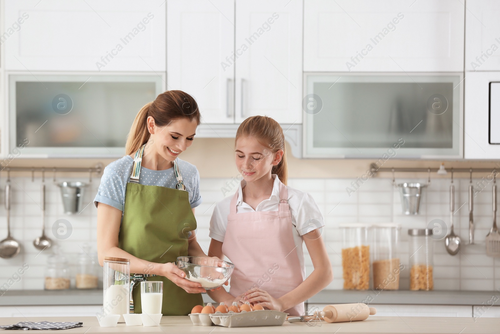 Photo of Mother and her daughter making dough at table in kitchen