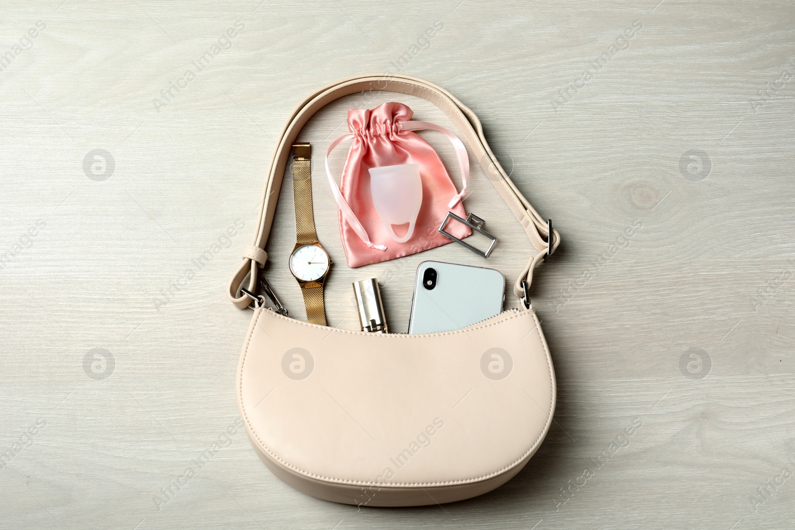 Photo of Menstrual cup and handbag with different women's accessories on white wooden table, flat lay
