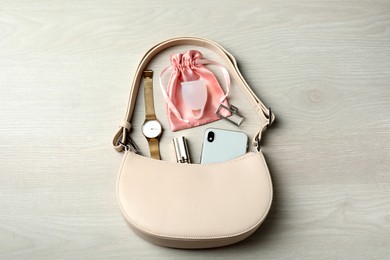 Photo of Menstrual cup and handbag with different women's accessories on white wooden table, flat lay