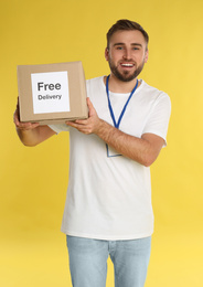Photo of Male courier holding parcel with sticker Free Delivery on yellow background