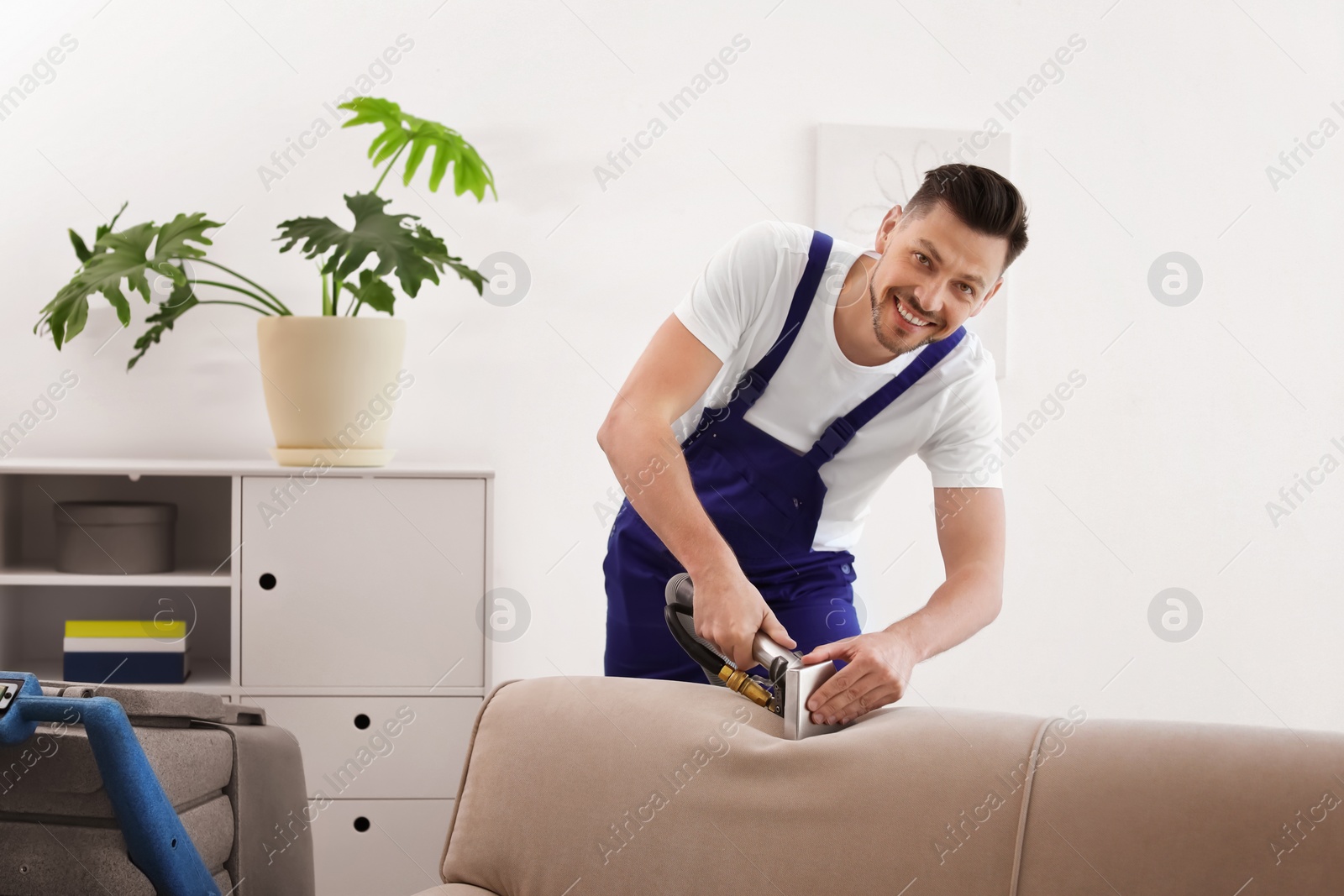 Photo of Dry cleaning worker removing dirt from sofa indoors