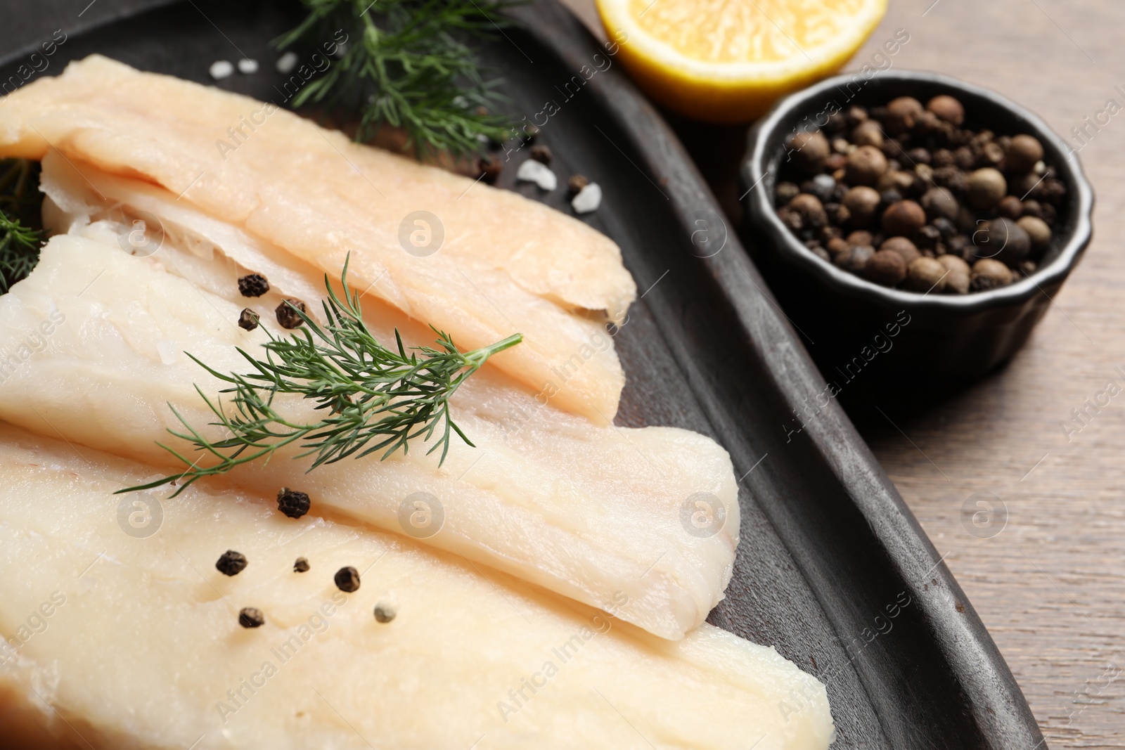 Photo of Raw cod fish, dill and spices on wooden table, closeup