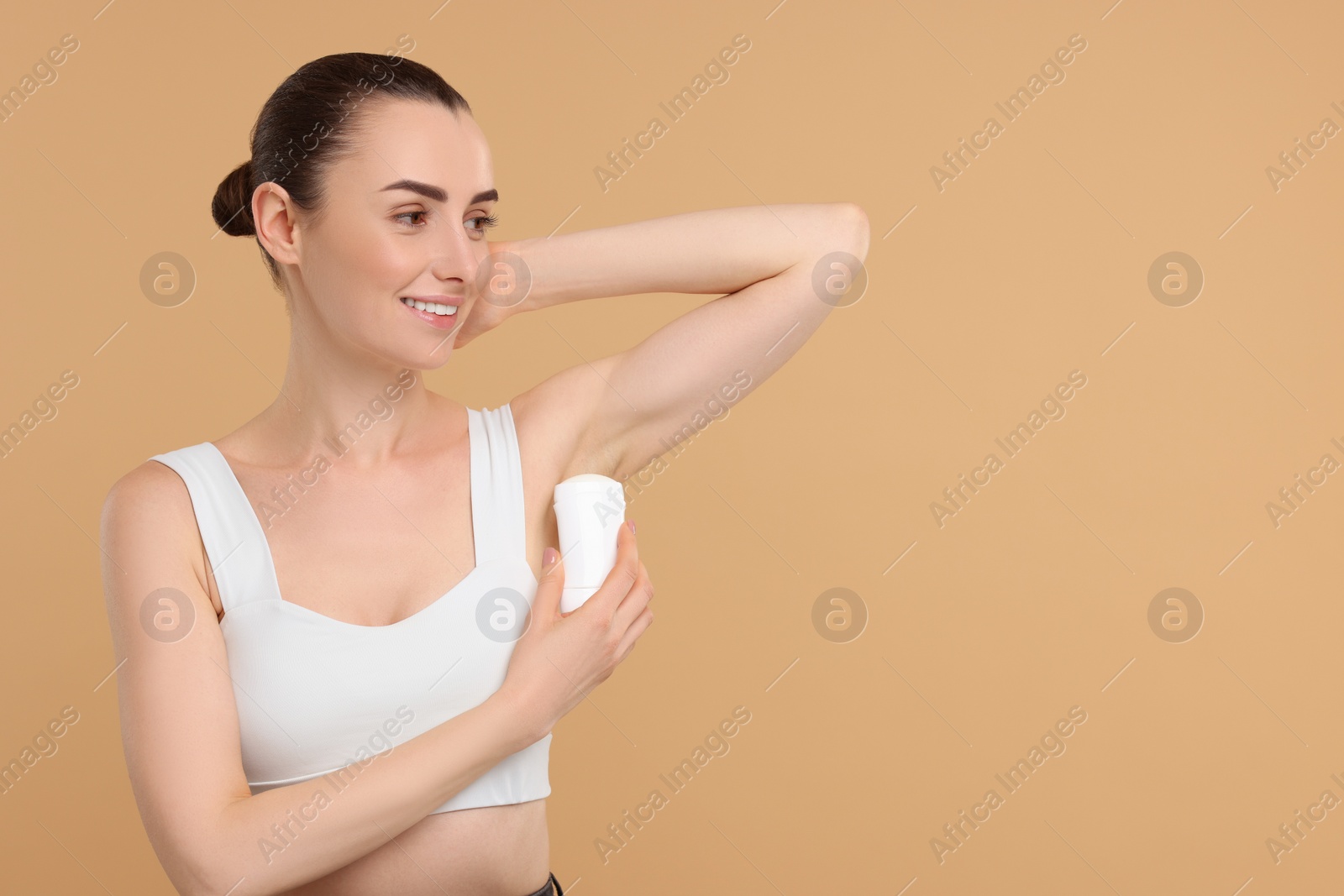 Photo of Beautiful woman applying deodorant on beige background, space for text