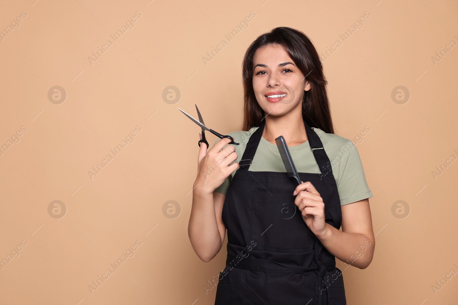 Photo of Portrait of happy hairdresser with professional scissors and comb against pale orange background. Space for text