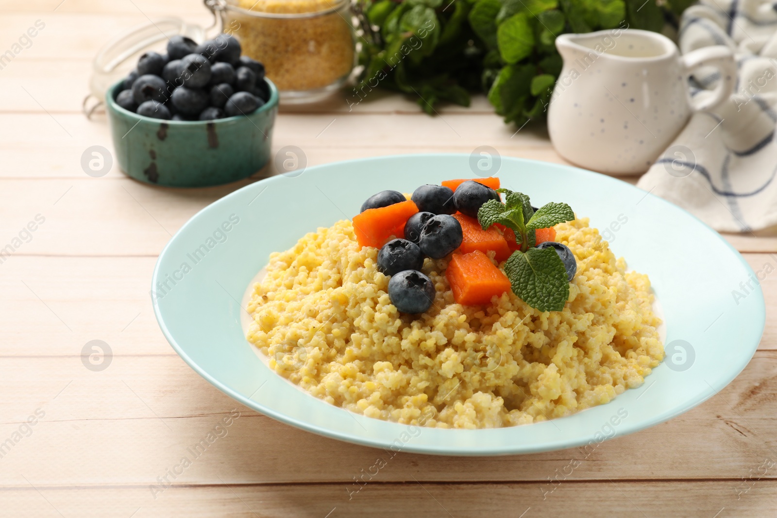 Photo of Plate with tasty millet porridge, blueberries, pumpkin and mint on light wooden table