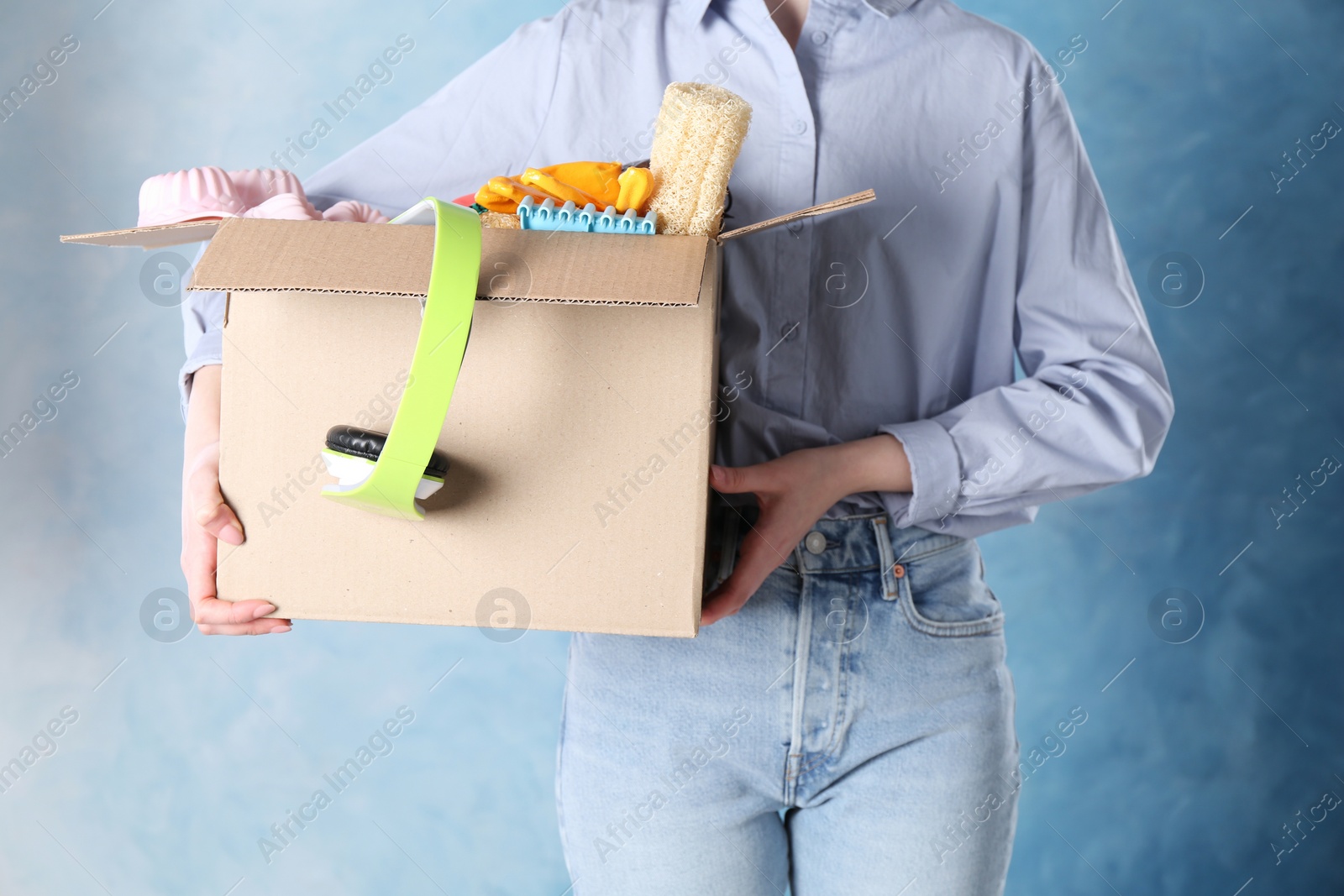 Photo of Woman holding box of unwanted stuff on blue background, closeup
