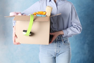 Photo of Woman holding box of unwanted stuff on blue background, closeup